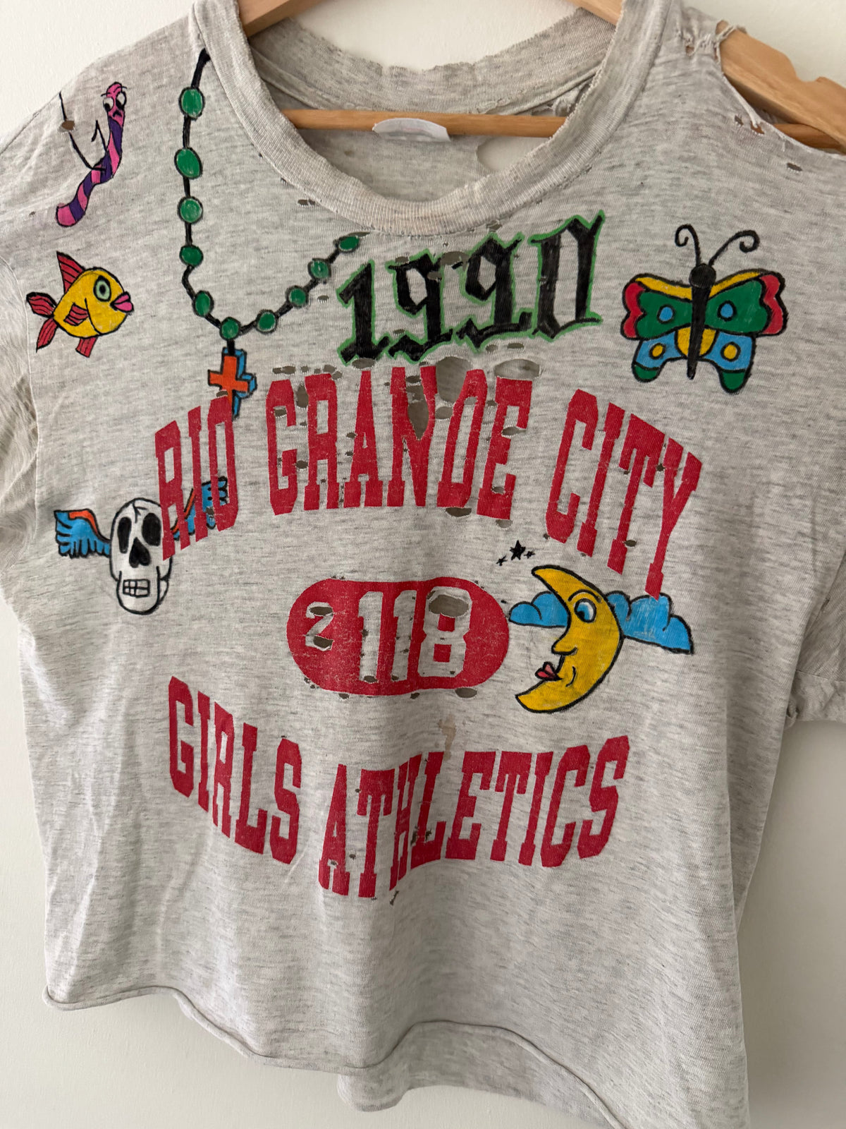Elephant Man Original Champion tee graphic close up showing rosary necklace butterfly fish skull moon and cross illustrations around collegiate lettering