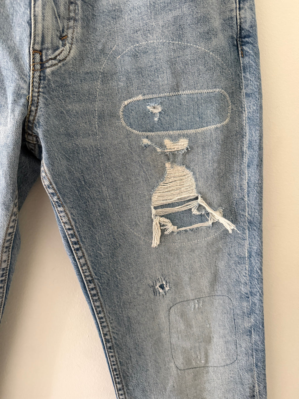Vintage Levi's 511 right thigh close up showing large oval hand-stitched repair with sculptural blown-out hole and dangling warp threads