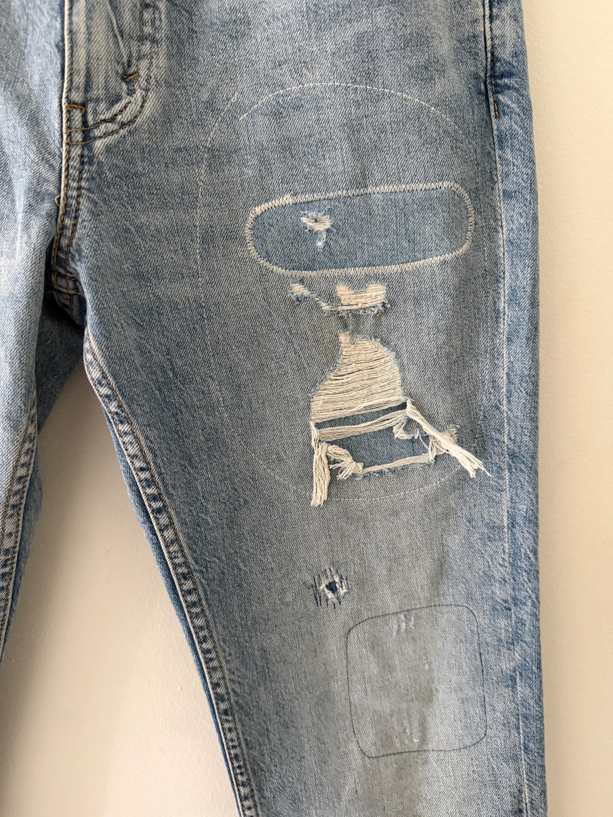 Vintage Levi's 511 right thigh close up showing large oval hand-stitched repair with sculptural blown-out hole and dangling warp threads