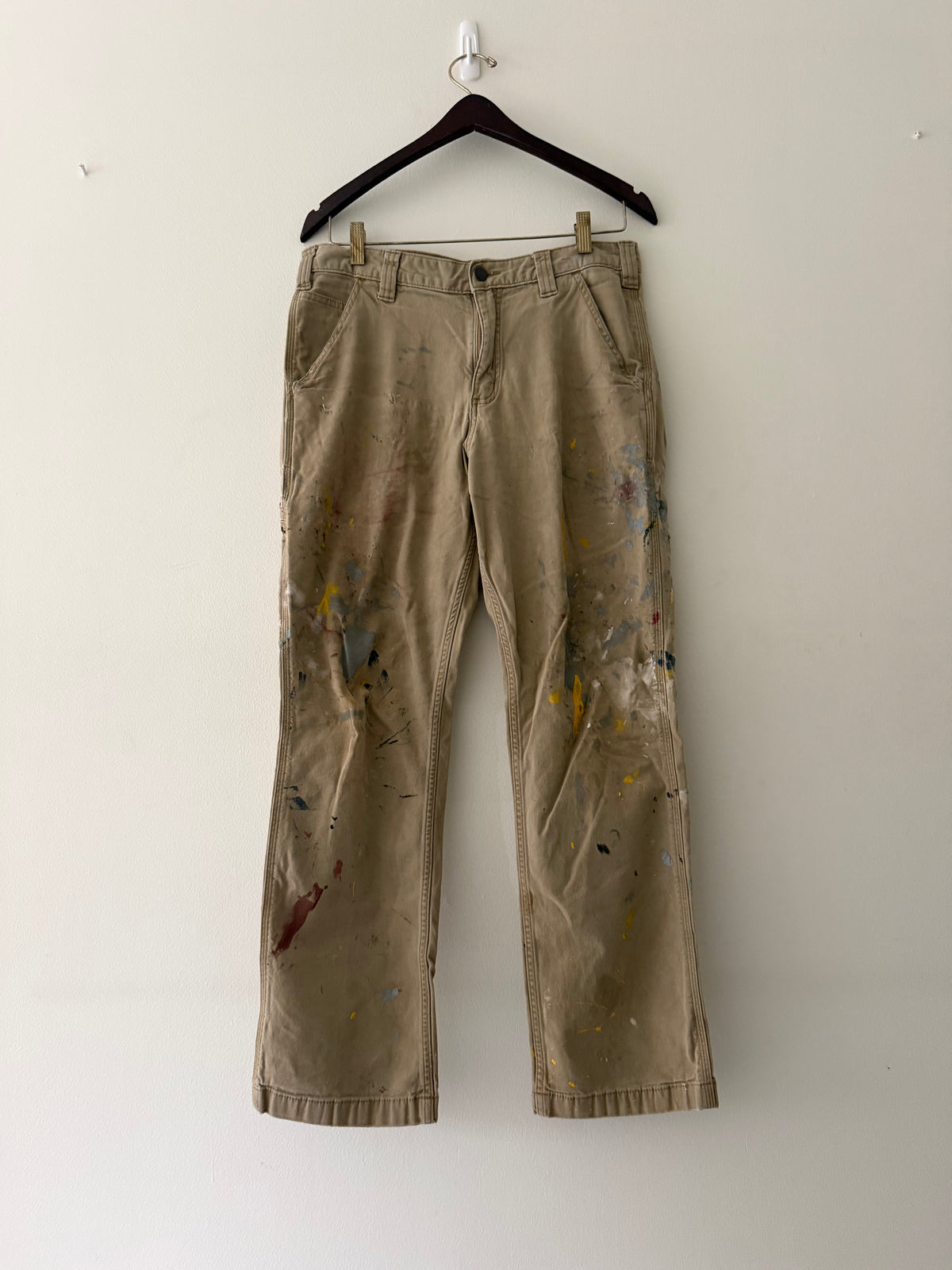 Vintage Carhartt carpenter pants back right pocket close up showing weathered C logo patch with handprint smears and paint