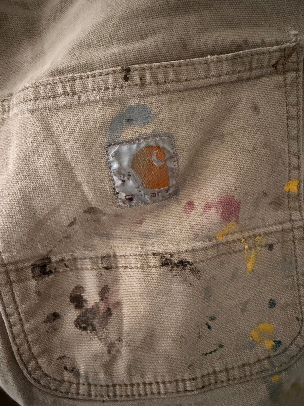 Vintage Carhartt paint-splattered carpenter pants front view showing khaki canvas with multicolor paint splatter throughout