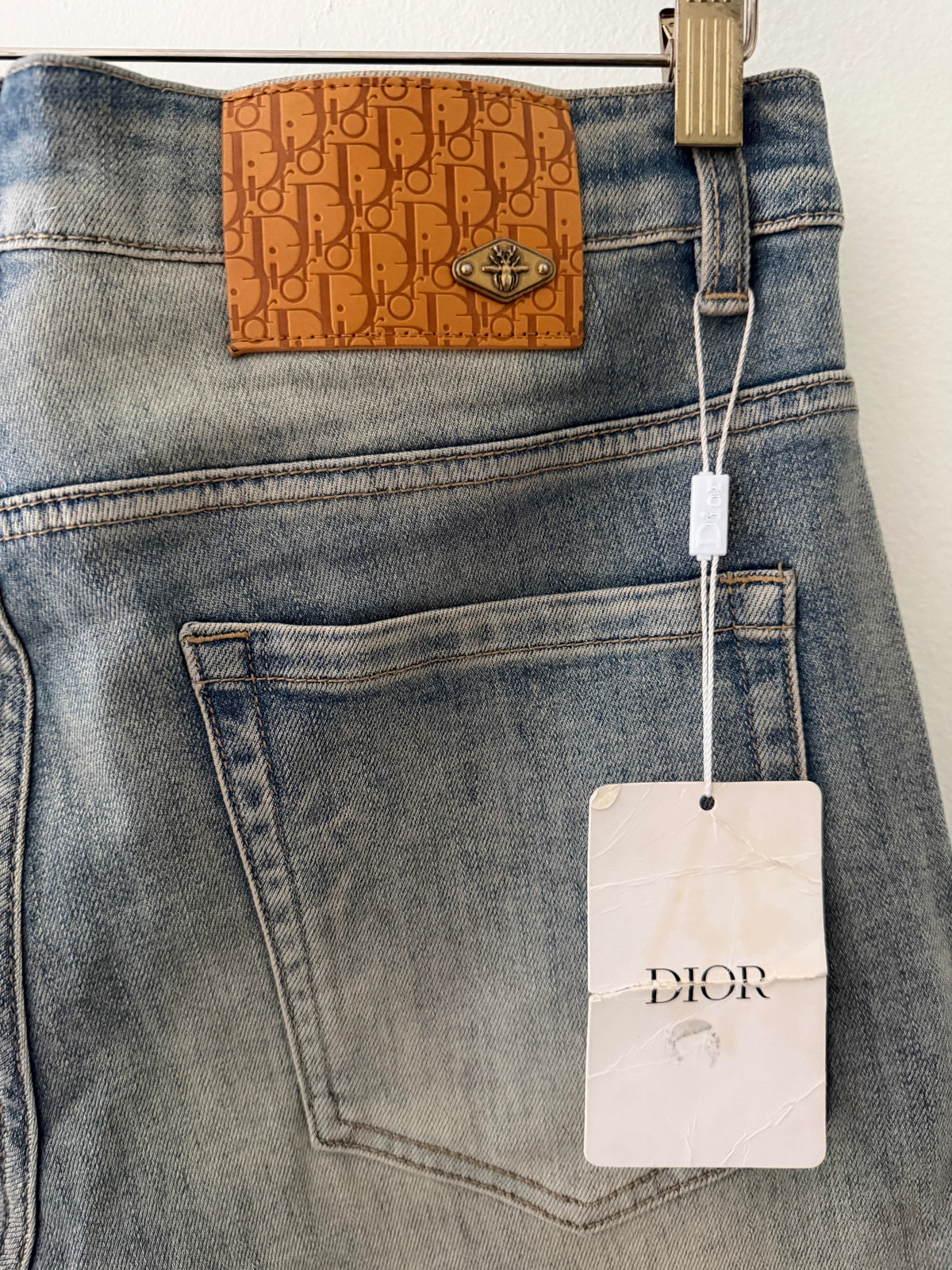 Dior Oblique monogram leather patch close up showing caramel tan patch with gold bee rivet and Dior hang tag on security wire
