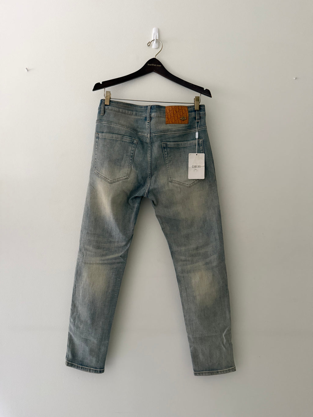 Dior mud-washed denim back view showing Oblique monogram leather patch with gold bee hardware and original Dior hang tag
