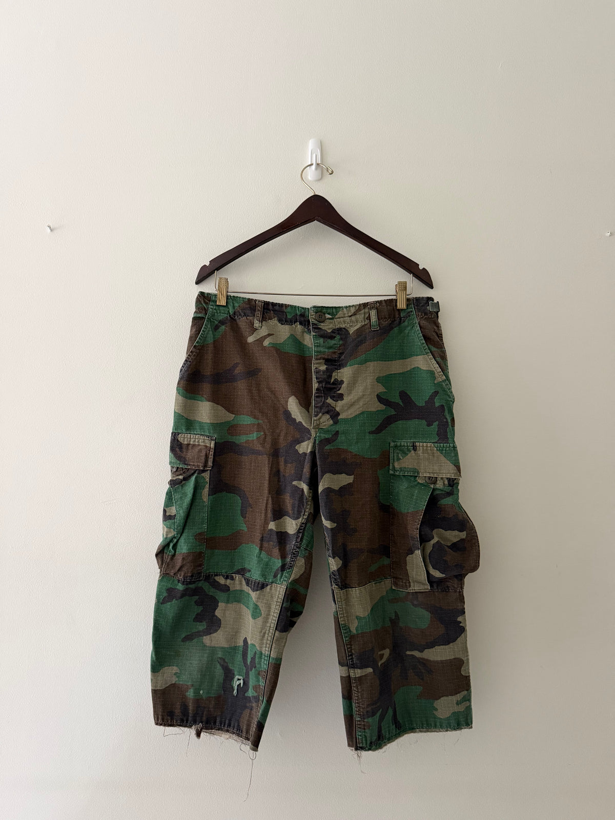 Vintage US military woodland camo raw edge cargo shorts front view showing six-pocket construction and fraying hem